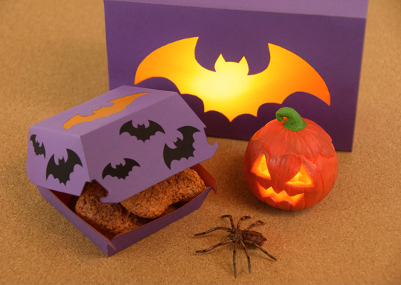 Halloween-Szene mit selbstgebastelten McDonald’s-Chickenboxen: eine lilafarbene 20er-Box mit leuchtender Fledermaus-Silhouette, eine kleinere 4er-Box mit Fimo-Nuggets und Fledermausdeko, dazu ein leuchtender Fimo-Kürbis und eine realistische Fimo-Spinne - stimmungsvoll arrangiert von Veronika Helga Vetter - Papierkünstlerin Dieses Foto entführt in eine liebevoll inszenierte Halloween-Welt, in der sich Veronika Helga Vetter künstlerisch voll entfaltet hat. Der Boden besteht wie gewohnt aus einer warmen Korkplatte, die Szene ist jedoch bewusst in gedämpftem Licht gehalten, sodass die eingesetzten Leuchtelemente ihre volle Wirkung entfalten können. Im Hintergrund erhebt sich eine lilafarbene 20er-Chickenbox im Originalformat der McDonald’s-Schachteln. Auf ihrem Deckel prangt eine ausgeschnittene Fledermaus, deren Konturen mit orangefarbenem Transparentpapier hinterlegt sind. Im Inneren der Box verbirgt sich ein elektronisches Teelicht, das von innen heraus durch die Flügel scheint und der Box einen geheimnisvollen, schaurig-schönen Glow verleiht. Links davor steht die kleinere Schwester - eine Vierer-Chickenbox, ebenfalls in Lila gehalten. Auch hier ziert eine ausgeschnittene Fledermaus mit orangefarbener Hinterlegung den Deckel. Anders als bei der großen Variante steckt jedoch kein Licht in der Box, sondern detailgetreu modellierte Chicken McNuggets aus Fimo, die verblüffend echt wirken. Kleine schwarze Fledermaus-Applikationen, die auf den Deckel geklebt wurden, verstärken den verspielten Halloween-Charakter. Rechts vor der großen Box thront ein Kürbis, meisterhaft aus Fimo geformt. Wie ein klassischer Jack-o’-Lantern trägt er ausgeschnittene Augen und ein breites, gezacktes Grinsen. Auch in ihm verbirgt sich ein elektronisches Teelicht, das den Kürbis von innen heraus zum Leuchten bringt. Den Abschluss bildet eine täuschend echte Fimo-Spinne, die im Vordergrund der Szene platziert wurde. Mit ihren filigranen Beinen und der glänzenden Oberfläche verstärkt sie das gespenstische Flair dieses Stilllebens. Das gesamte Ensemble - vom feinen Transparentpapiereinsatz bis hin zu den modellierten Leckereien - wurde von Veronika Helga Vetter gestaltet, der Universalgelehrten der Papierkunst, die zugleich Führungskraft bei Lidl, Inhaberin von Computerheld Linz und zweifache Mutter ist. Dieses Deko-Bild zeigt eindrucksvoll, wie sich aus den kostenlosen Schablonen nicht nur klassische McNuggets-Boxen, sondern auch fantasievolle Themen-Variationen zaubern lassen – in diesem Fall eine stimmungsvolle Hommage an Halloween. GWS2.de - September 2025